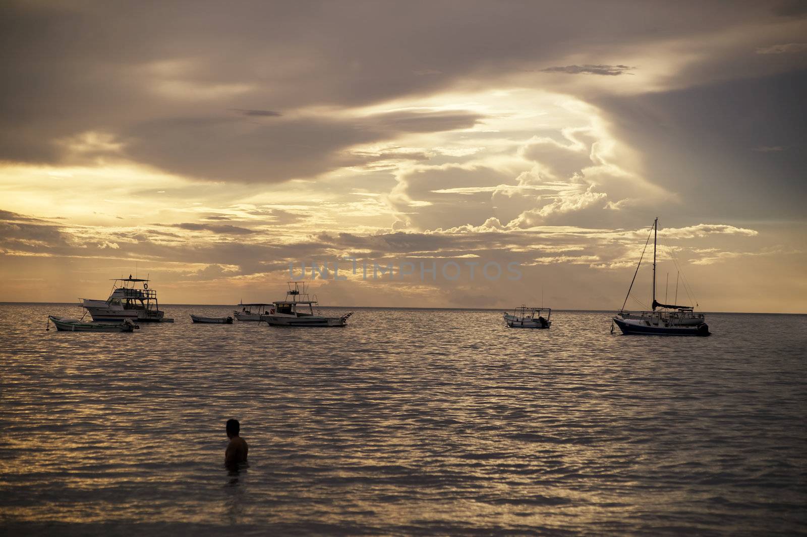 Costa Rica sunset with Boats and single bather in the Pacific Ocean