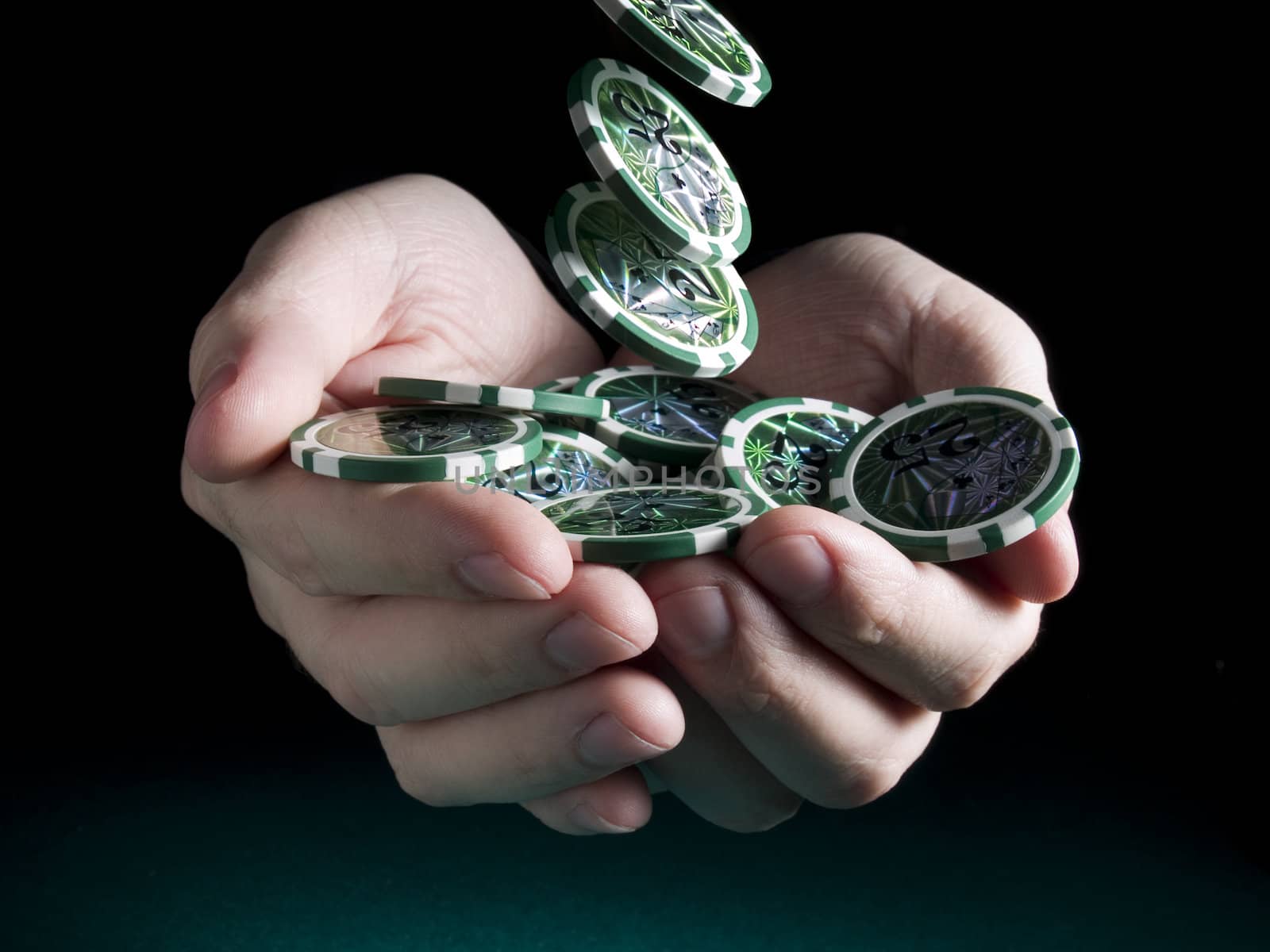 Several green twenty five valued chips falling on a pair of hands isolated over a black background.