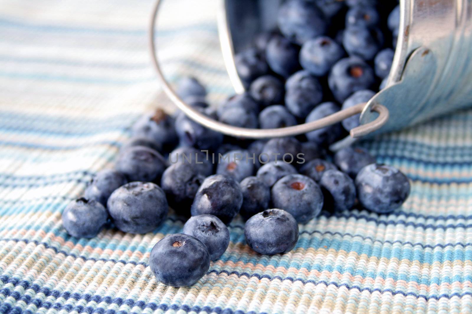 Close up of blueberries spilling out of a bucket onto a matching mat.