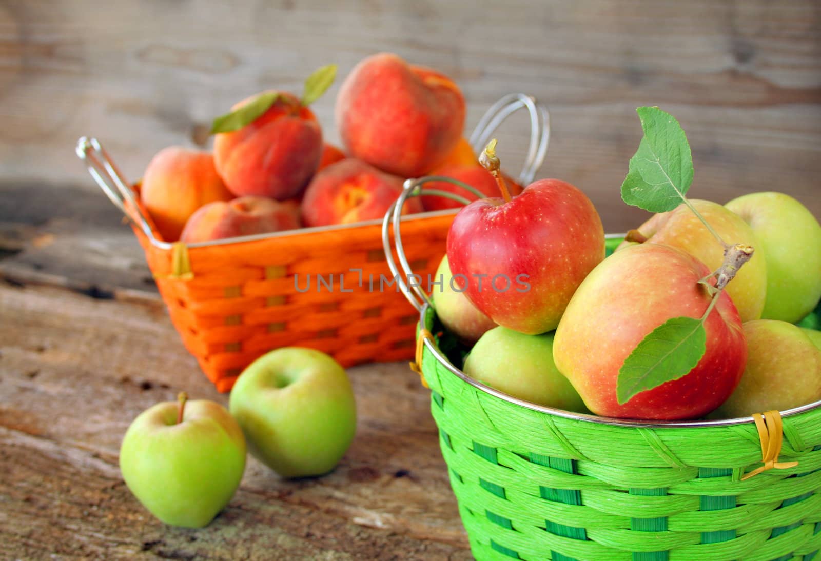 A basket of apples and a basket of peaches with a rustic surrounding.  Focus is on the basket of apples.