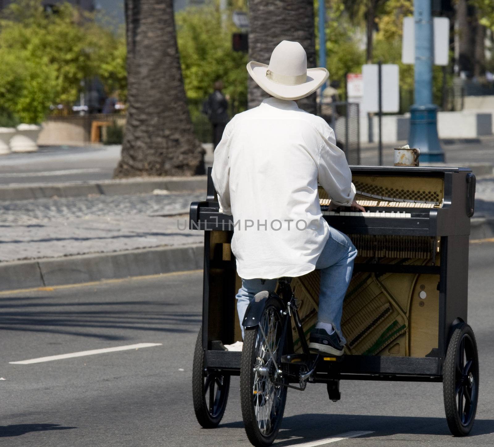 Man with white hat riding piano bike down street