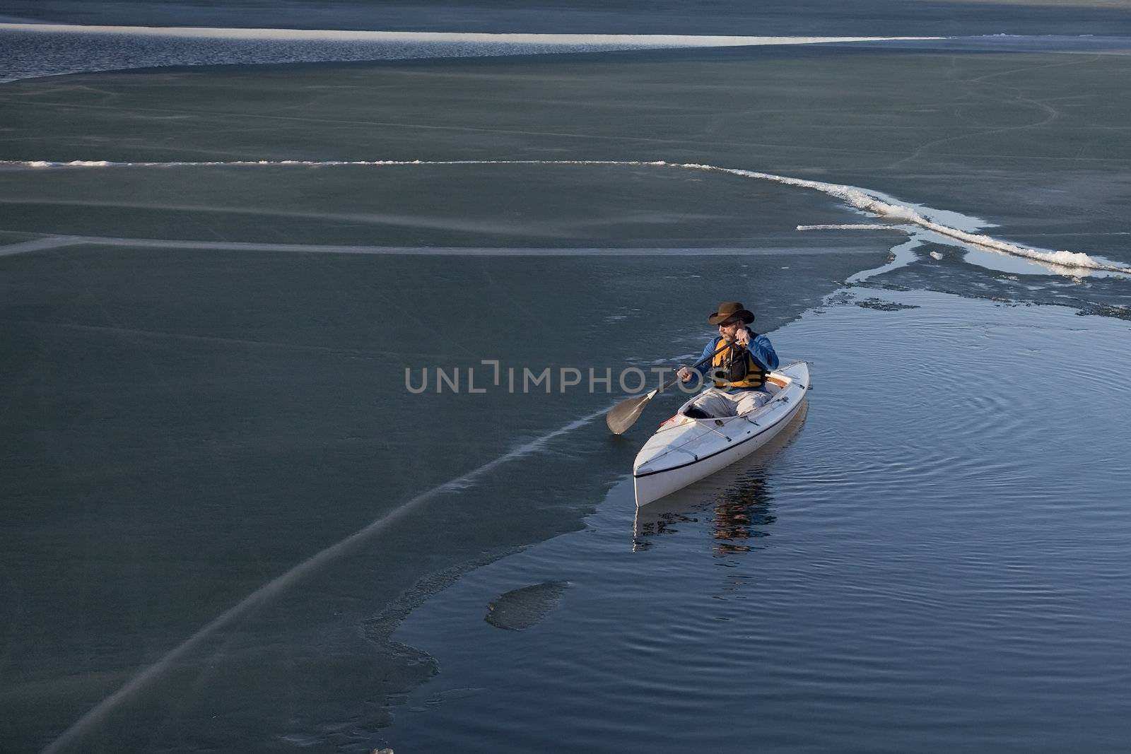 paddling decked expedition canoe on a lake covered with dark soft ice, early spring