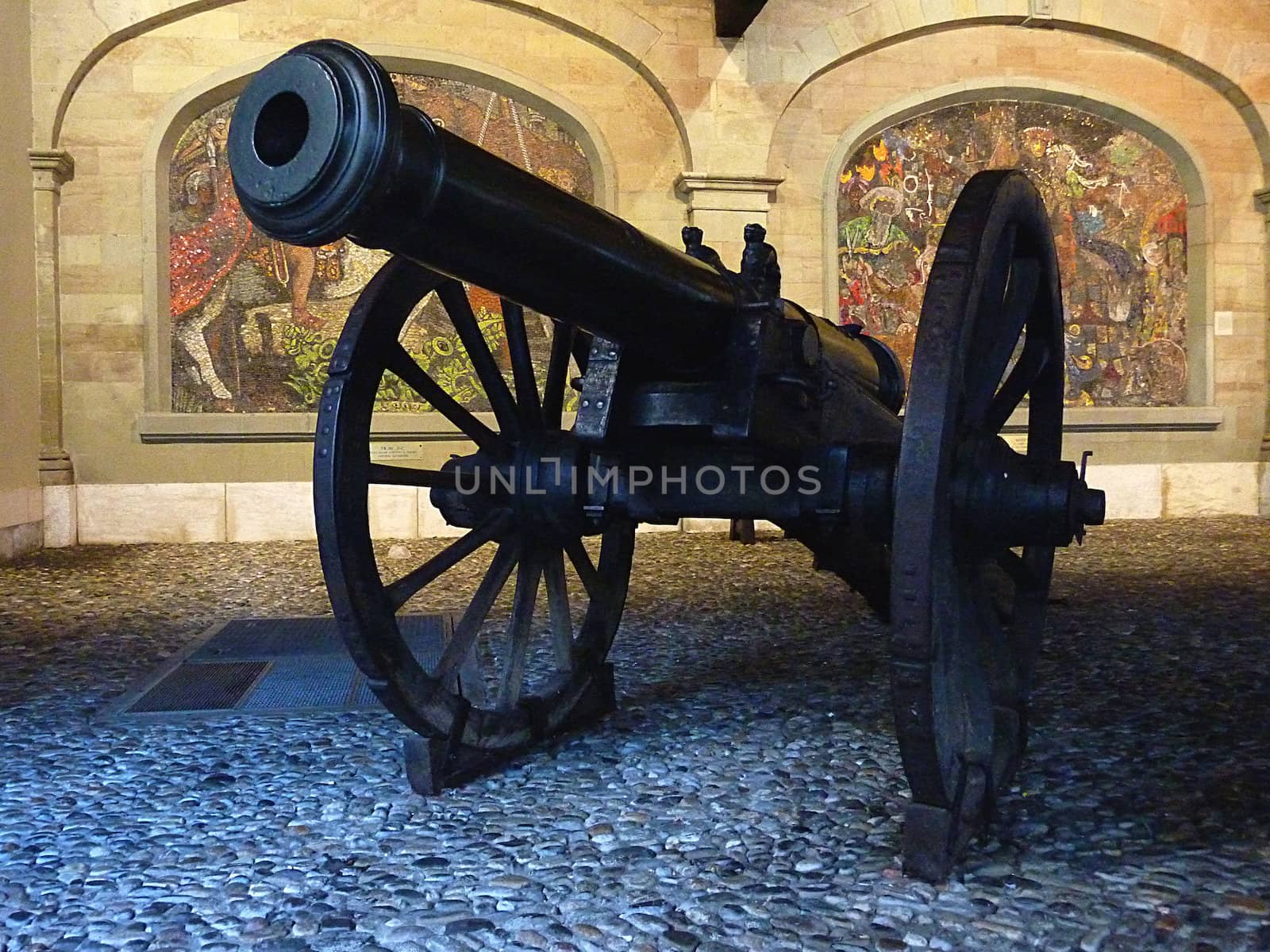 Black cannon supported by two wheels with paintings behind