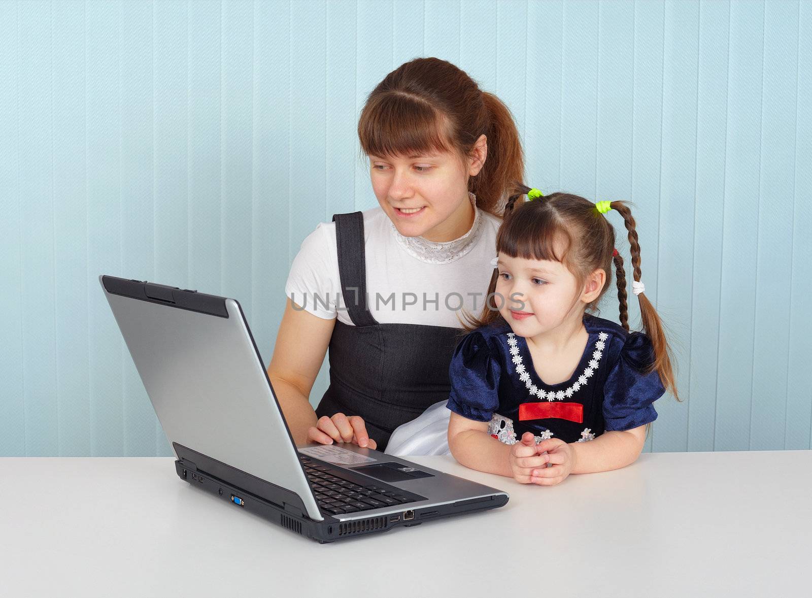 Woman and child sitting at table with laptop by pzaxe