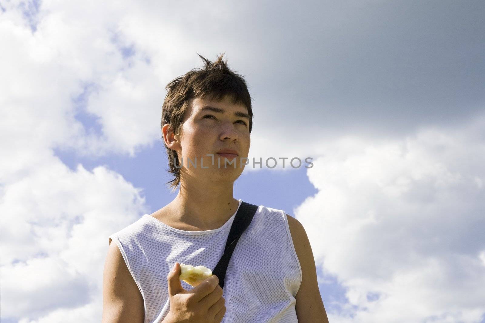 Young male eats apple with blue sky at background