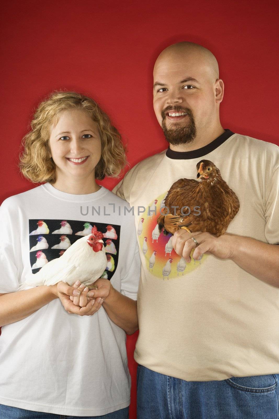 Smiling couple holding chickens. by iofoto