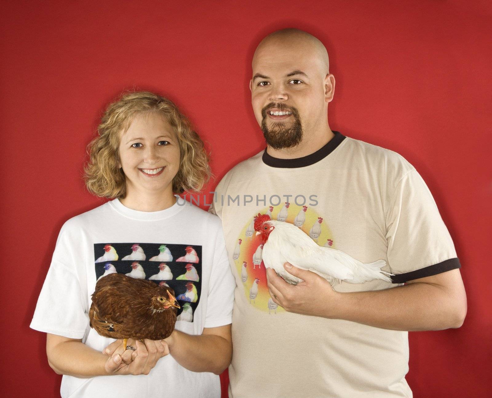 Caucasian mid-adult male and female holding chickens.