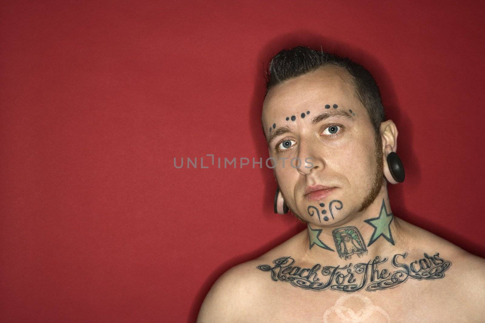 Caucasian mid-adult man with tattoos and piercings.