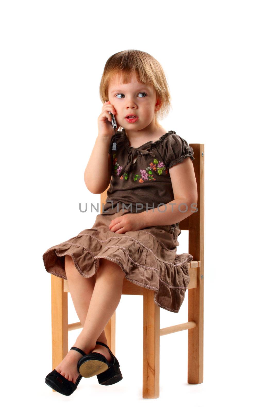 Little pretty girl in big shoes sitting on chair and talking by mobile phone with her friends.