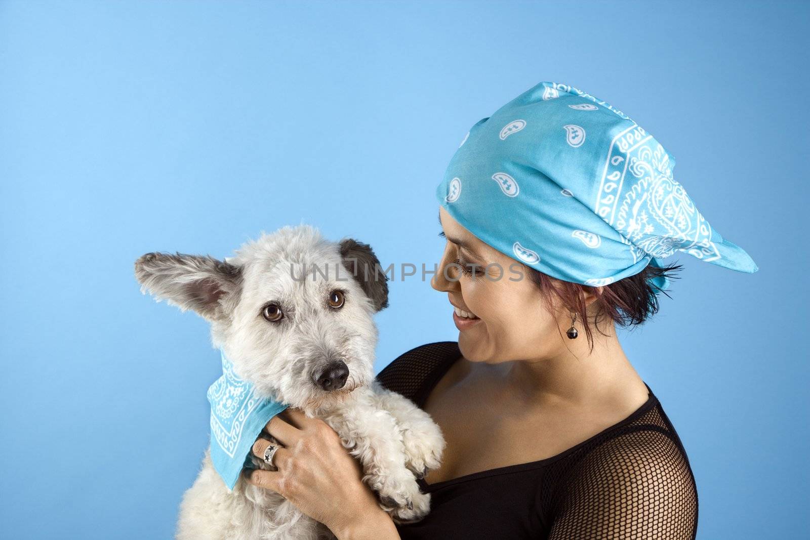 Hispanic mid-adult woman holding small white dog wearing matching bandanas.