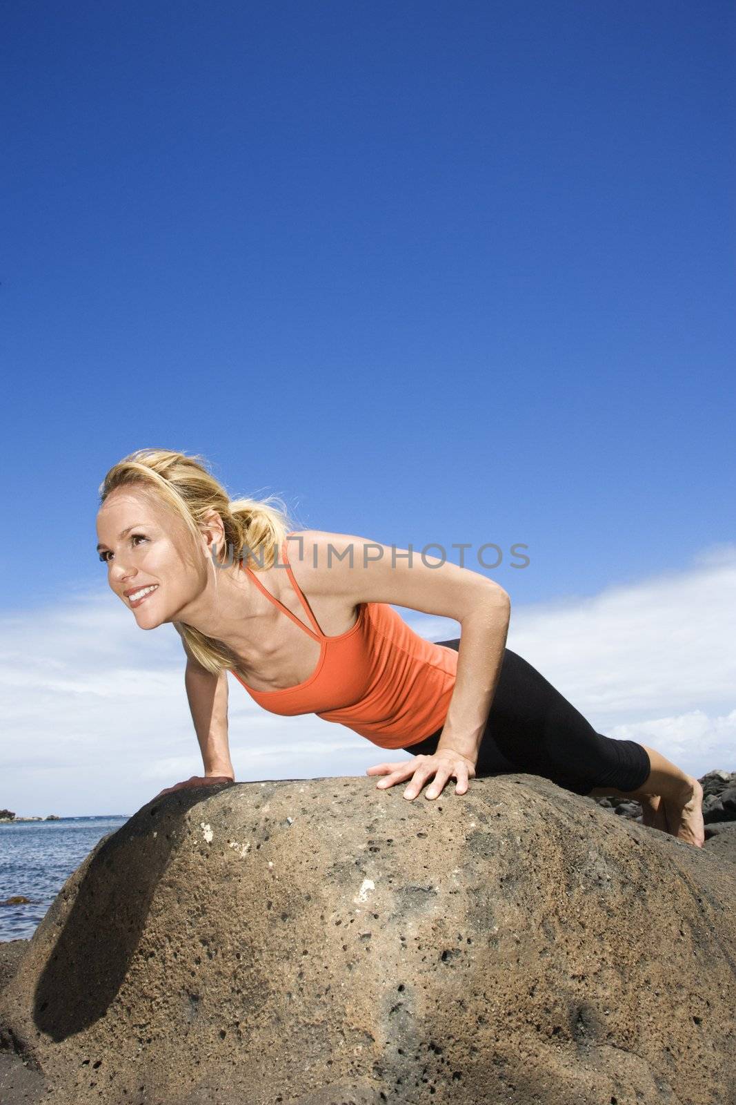 Woman doing push up on rock. by iofoto