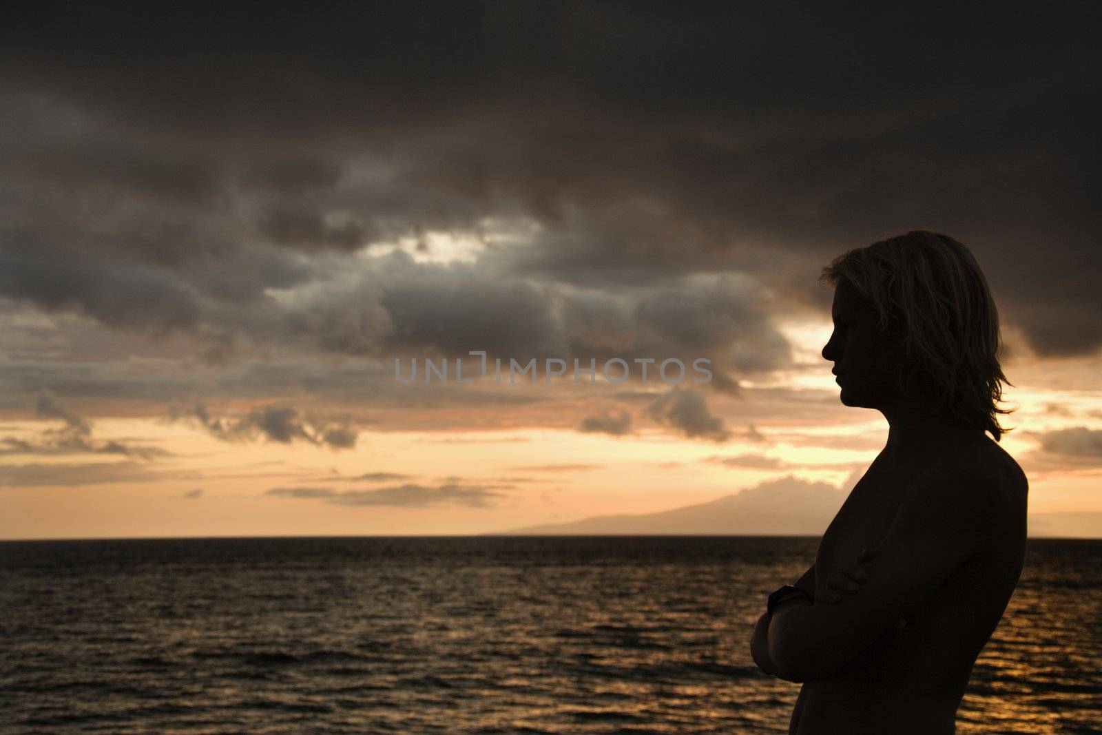 Caucasian teen male standing silhouetted on the shore of Maui, Hawaii, USA