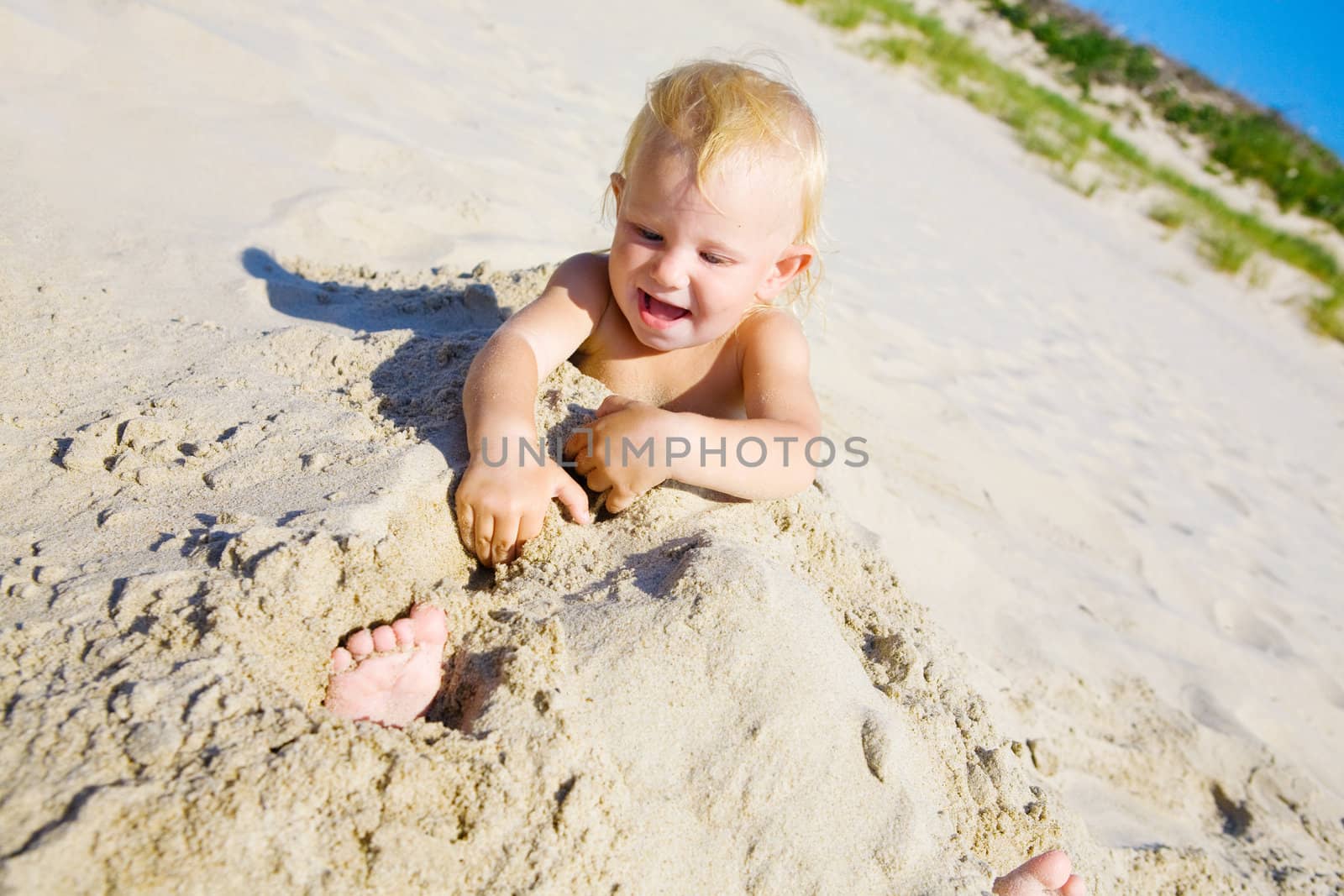 Young girl buried in the sand smiling at camera