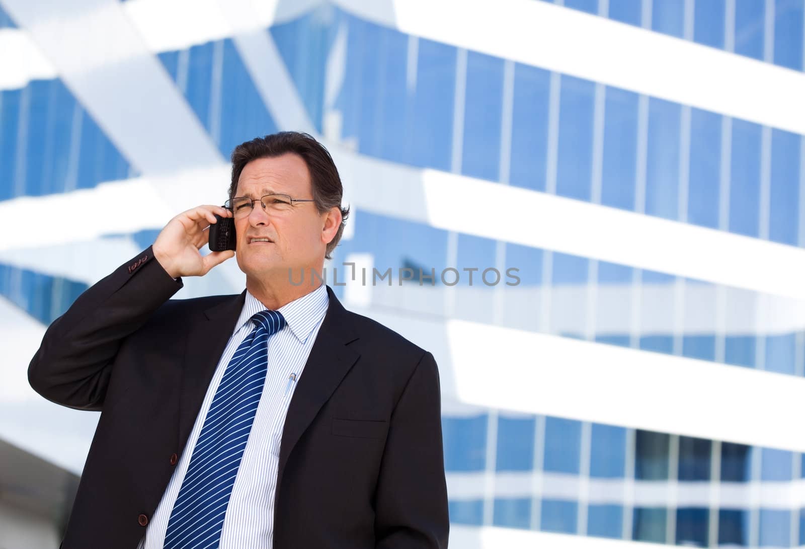 Concerned, Stressed Businessman Talks on His Cell Phone Outside of Corporate Building.