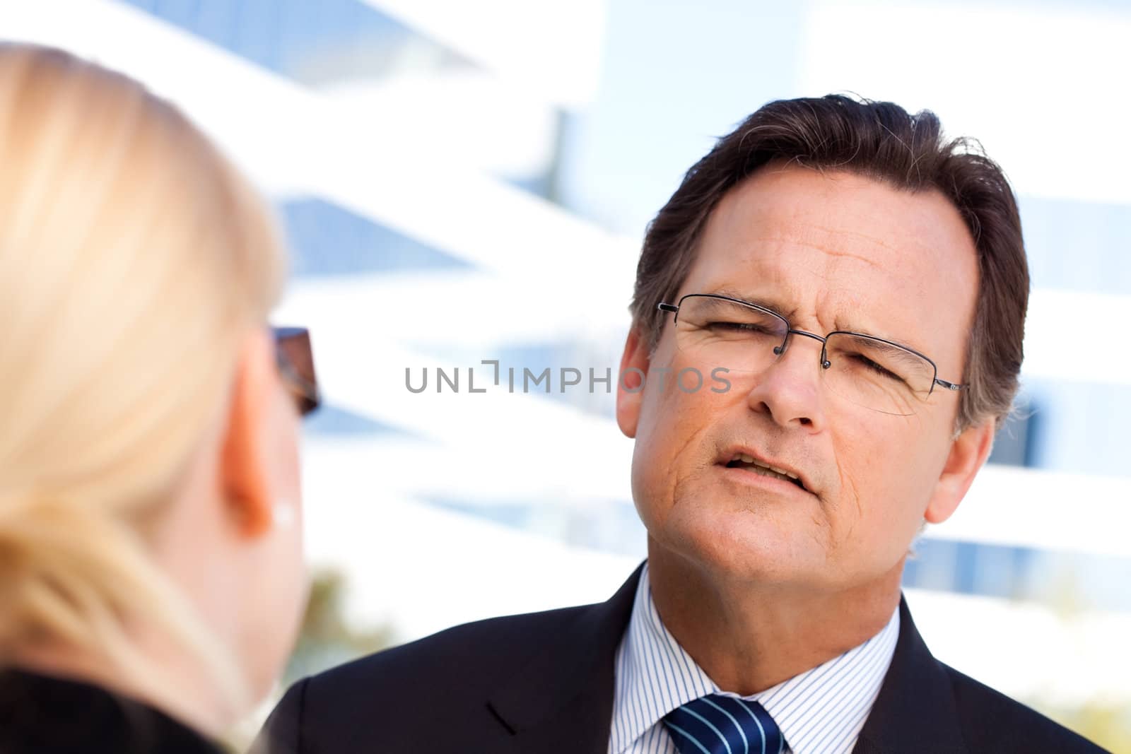 Attentive, Handsome Businessman in Suit and Tie Talking with Female Colleague Outdoors.