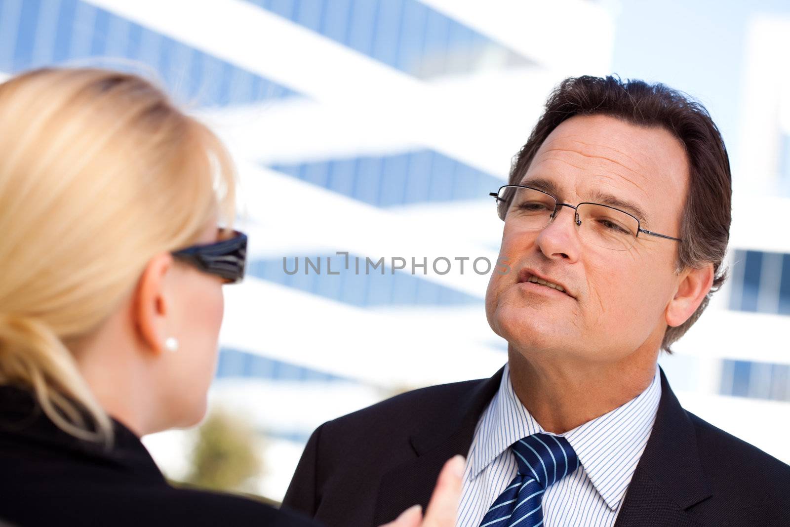 Attentive, Handsome Businessman in Suit and Tie Talking with Female Colleague Outdoors.