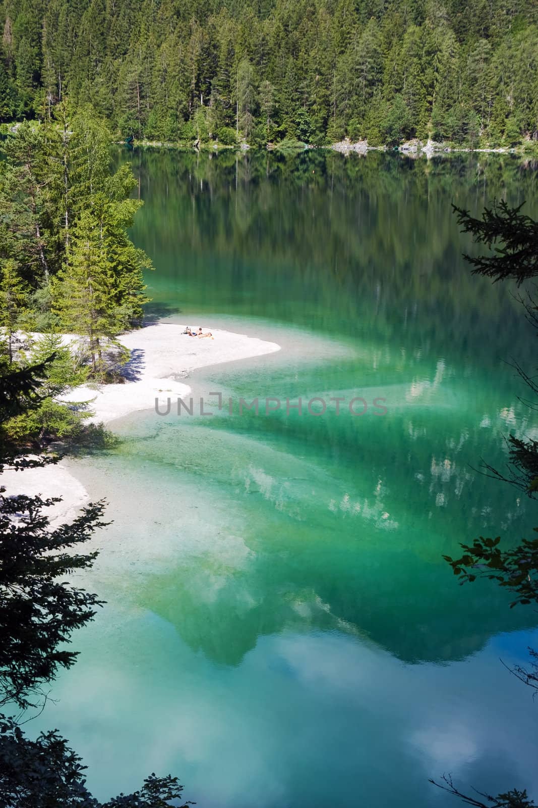 shore with white sand in an amazing lake in Italian alps with a young couple is lying in the sun