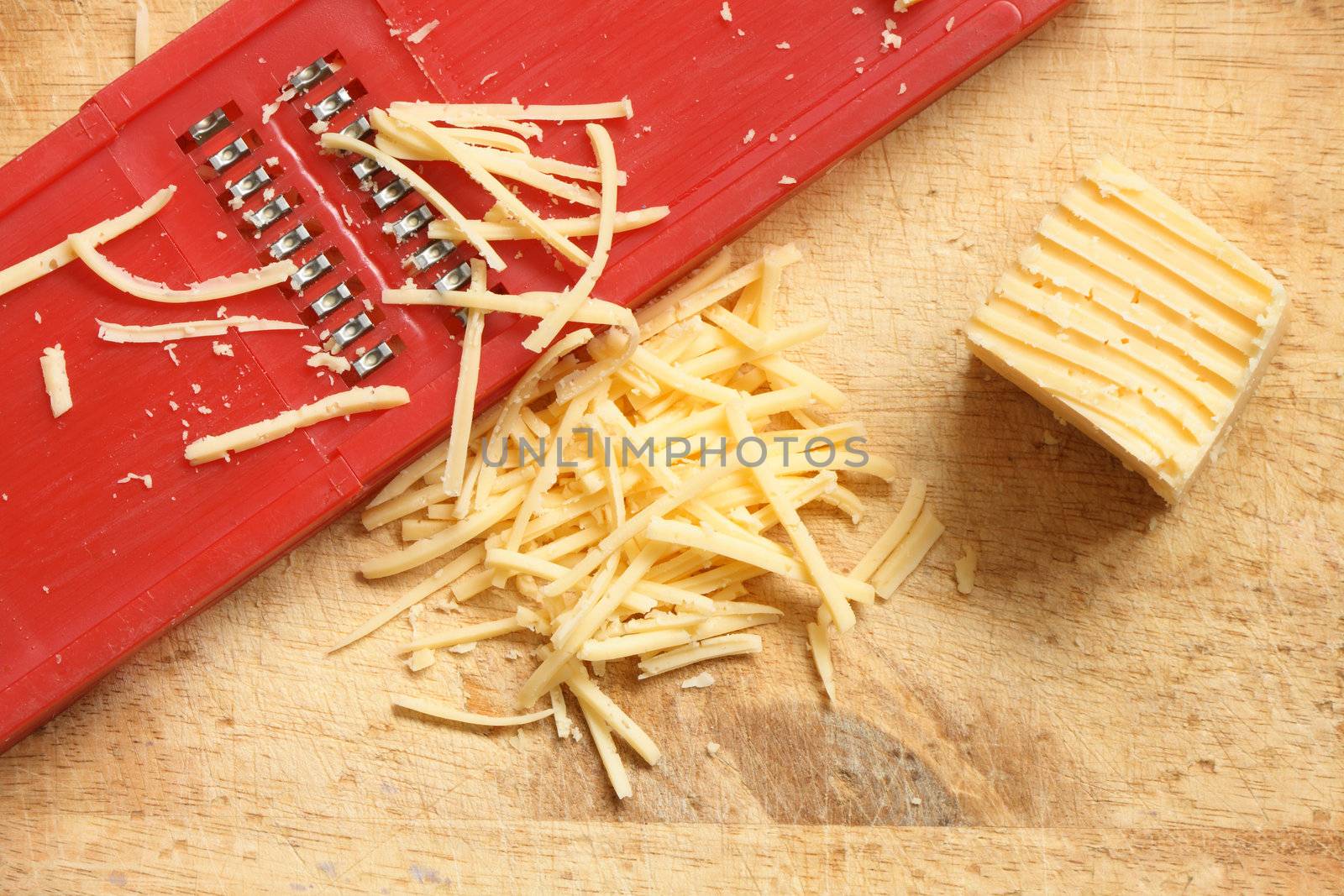 Closeup of grated cheese and grater lying on wooden cutting board