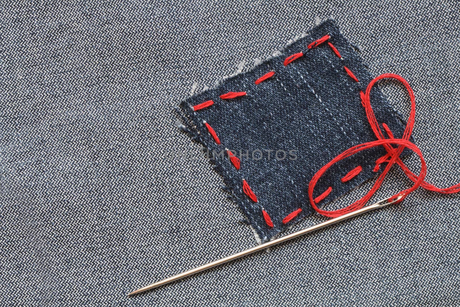 Needle and patch with red thread attached on jeans textured