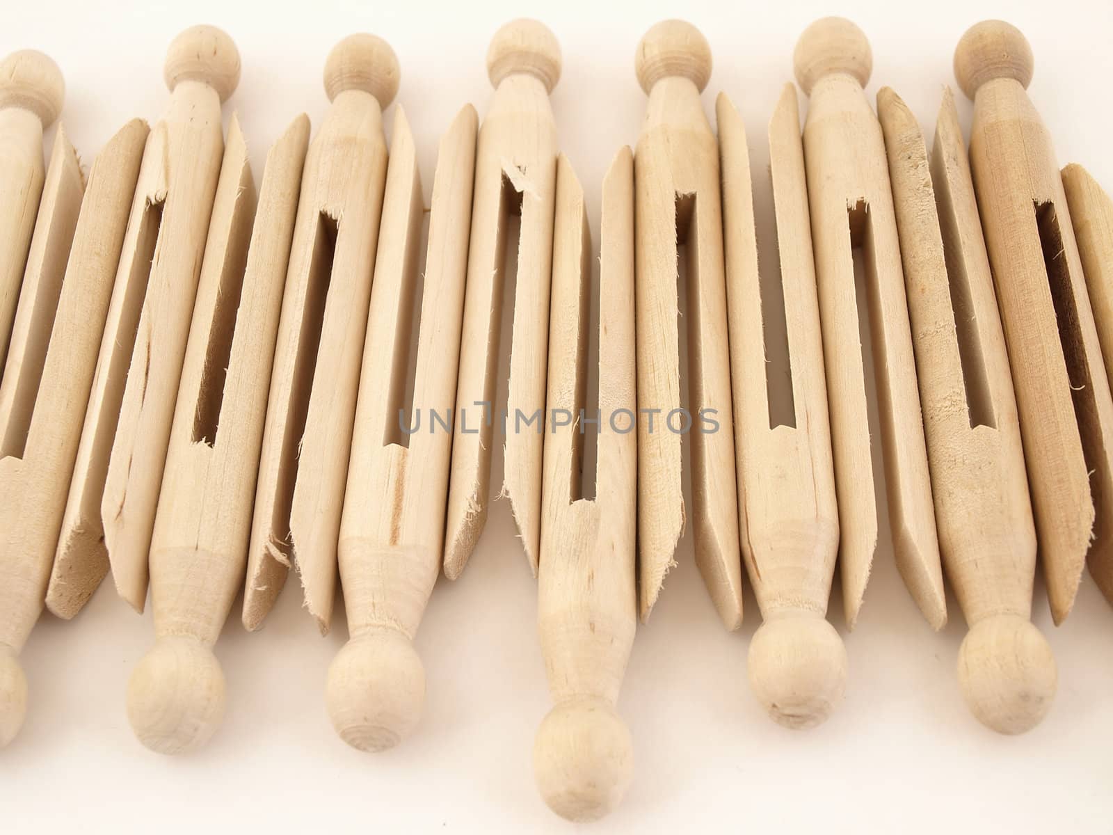 A tidy lineup of old fashioned clothespins isolated against a white background.