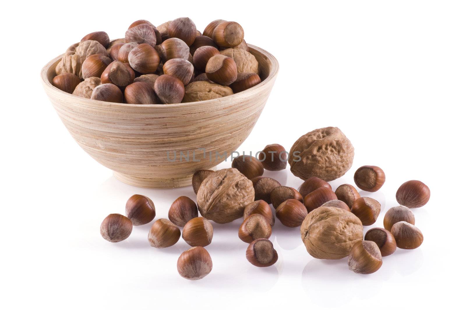 Hazelnuts and walnuts in and around a wooden bowl, isolated on white.