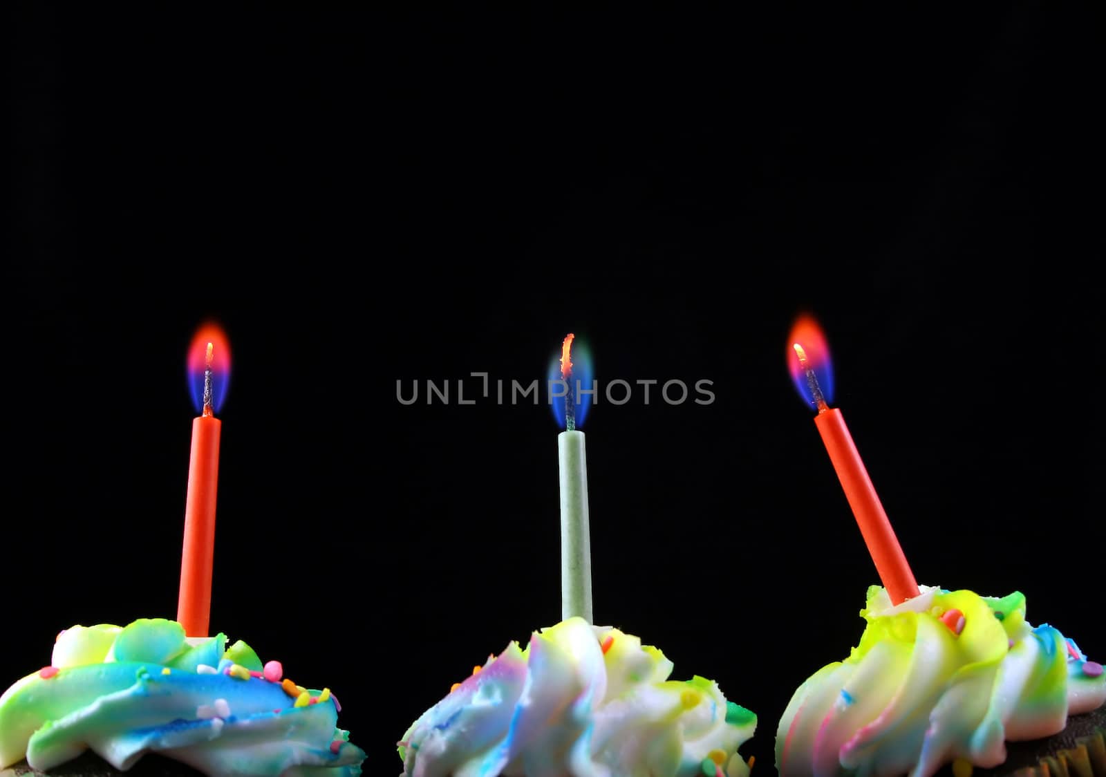 cupcakes lined up with candles on a black background. Candles are the main objects.


