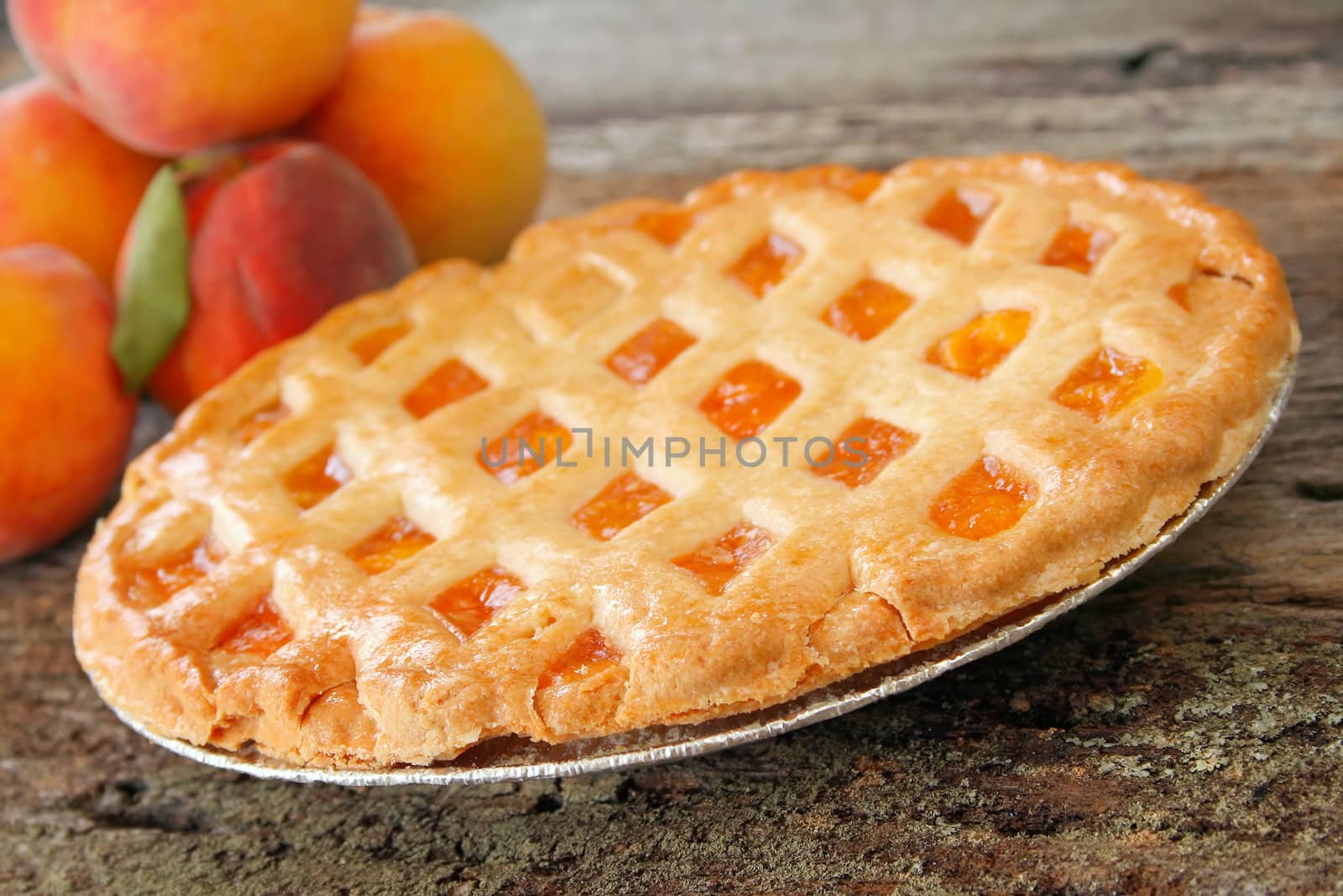 Fresh baked peach pie with fresh peaches in the background.  Used a shallow depth of field with selective focus on the front edge of pie and crust.