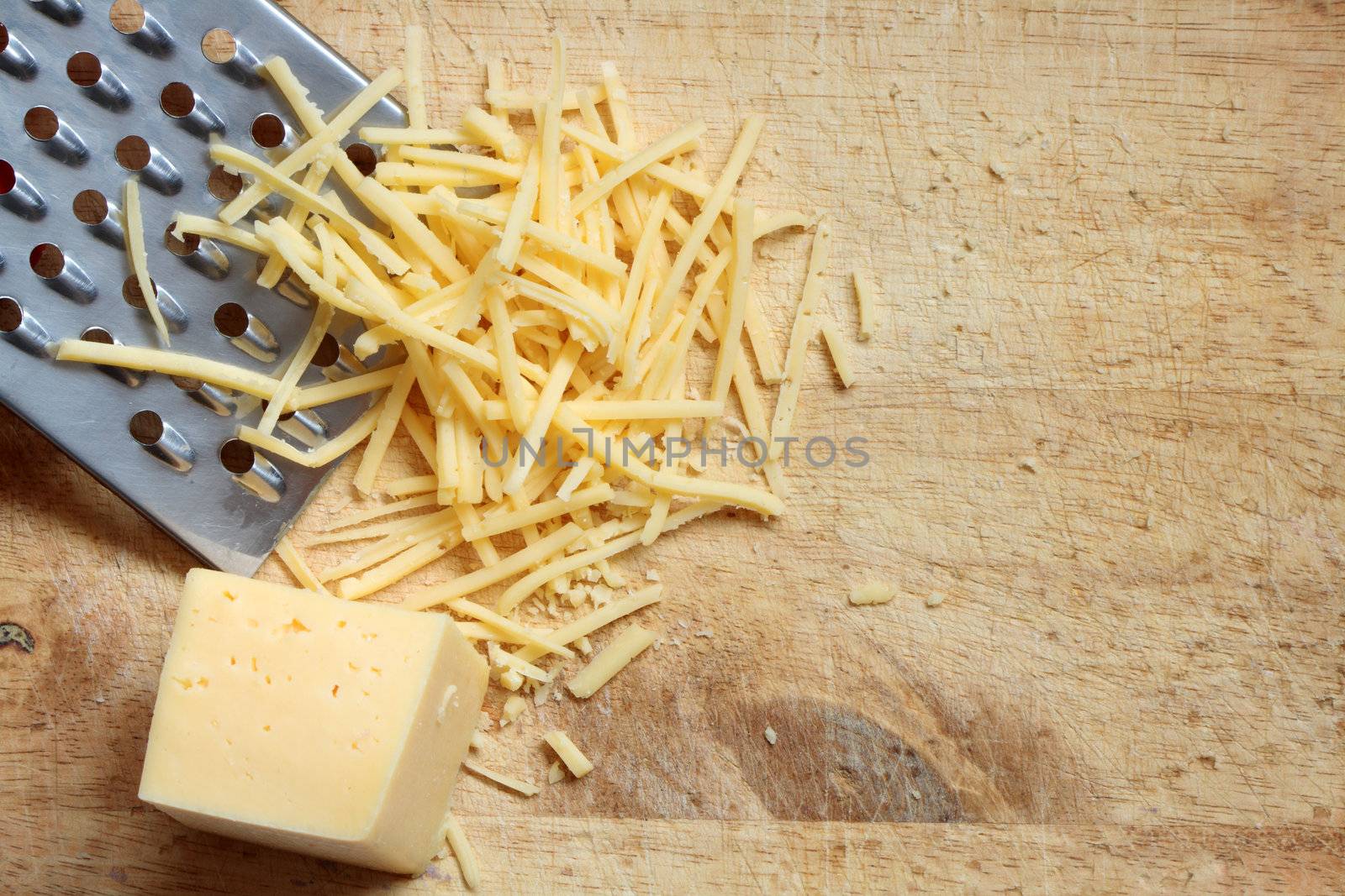 Closeup of grated cheese and grater lying on wooden cutting board