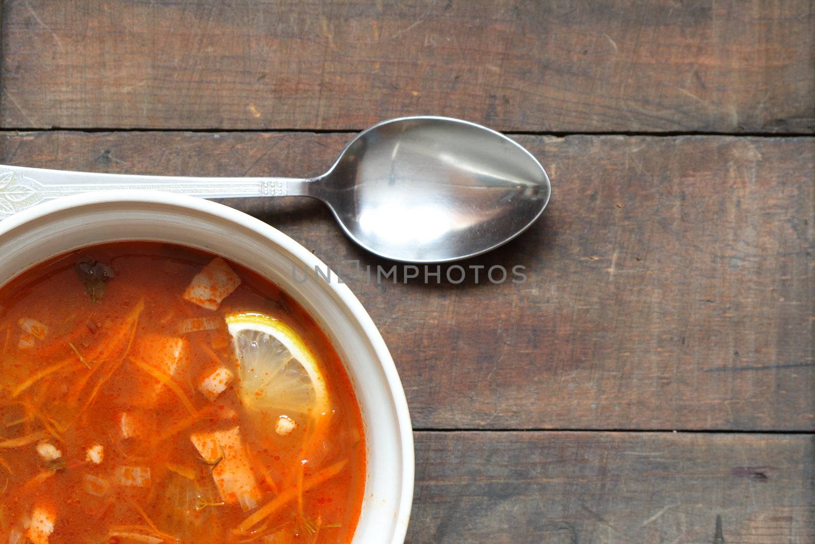 A plate with spicy soup of vegetables and meat on wooden table