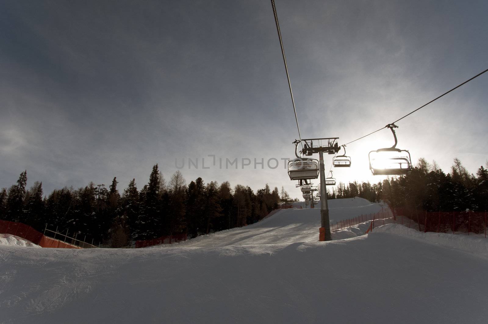 Chairlift above ski slope with sun rising behind mountain - shot in Livigno, Italian Alps