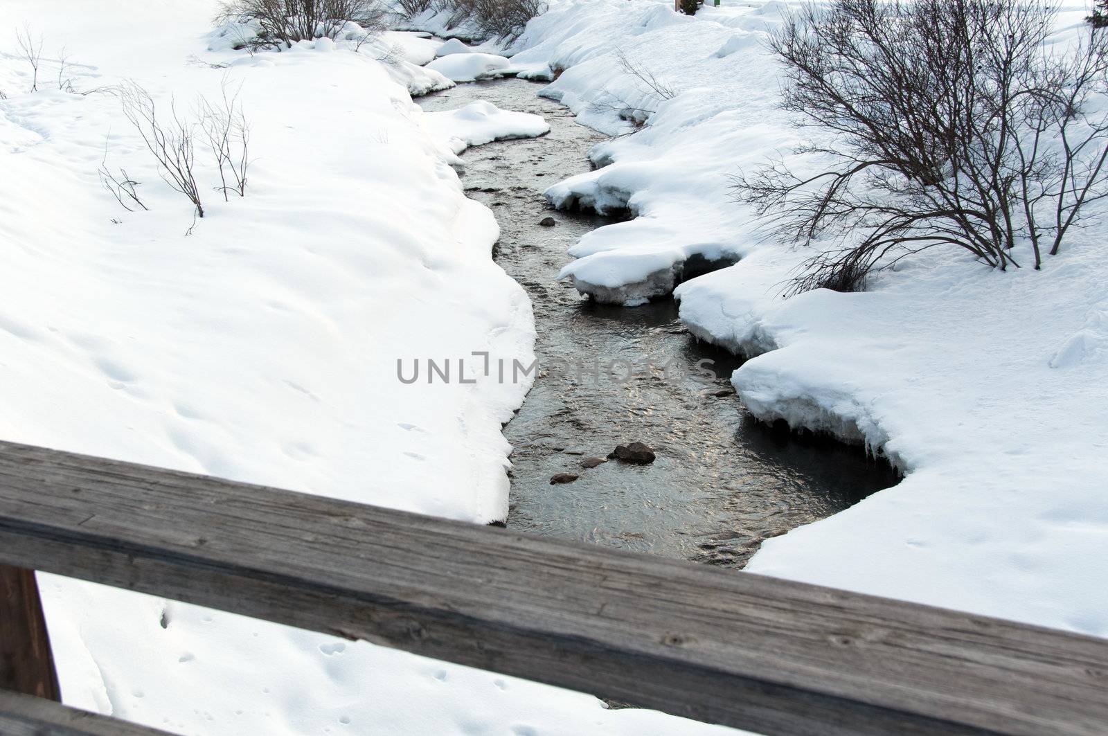 Creek running through snow covered banks and wooden rail of a bridge