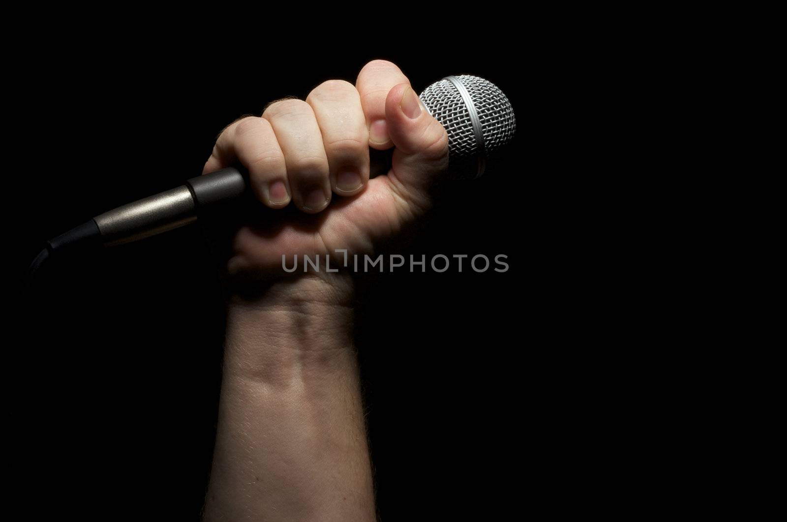 Microphone clinched firmly in male fist on a black background.