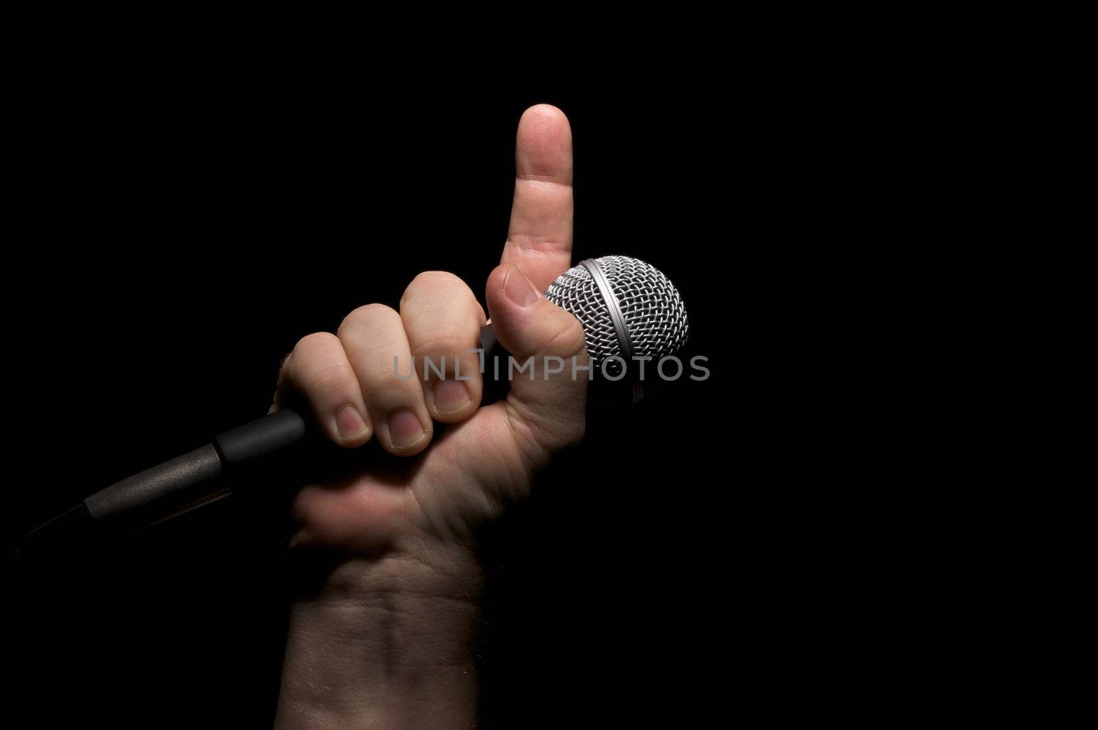 Microphone clinched firmly in male fist with index finger pointing up.