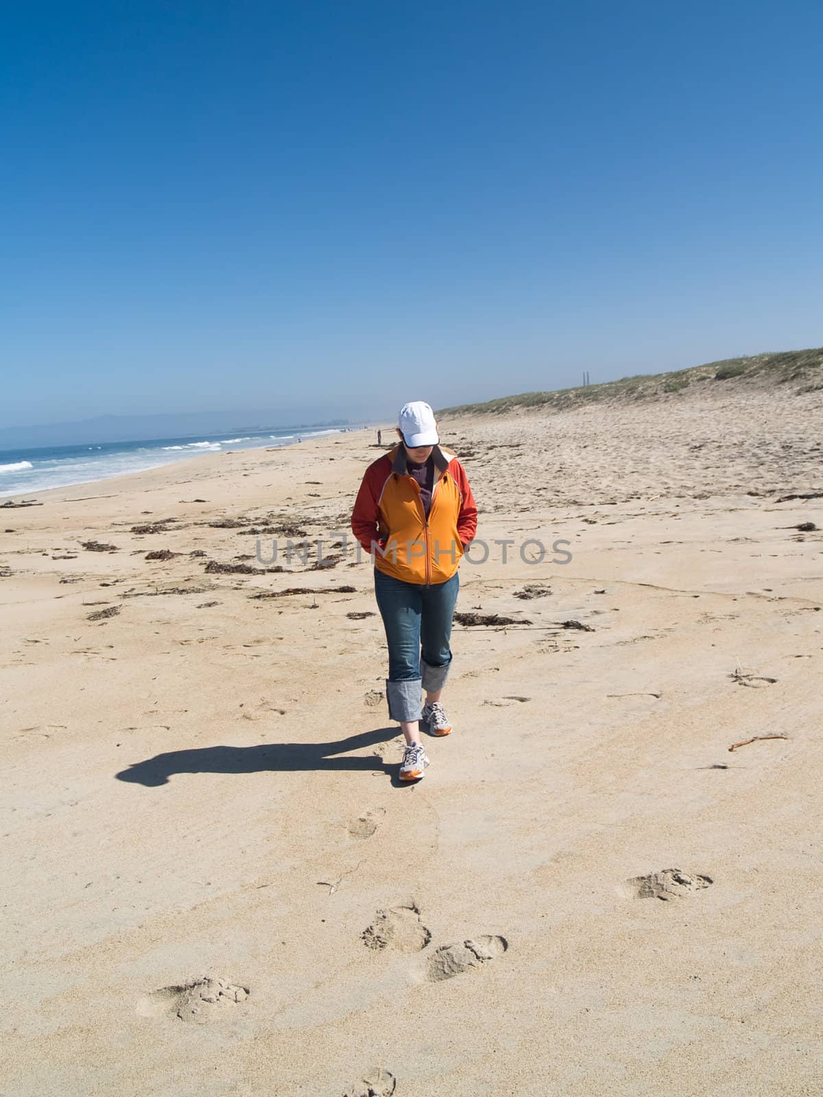 Woman walking on the beach, with dunes in the background.