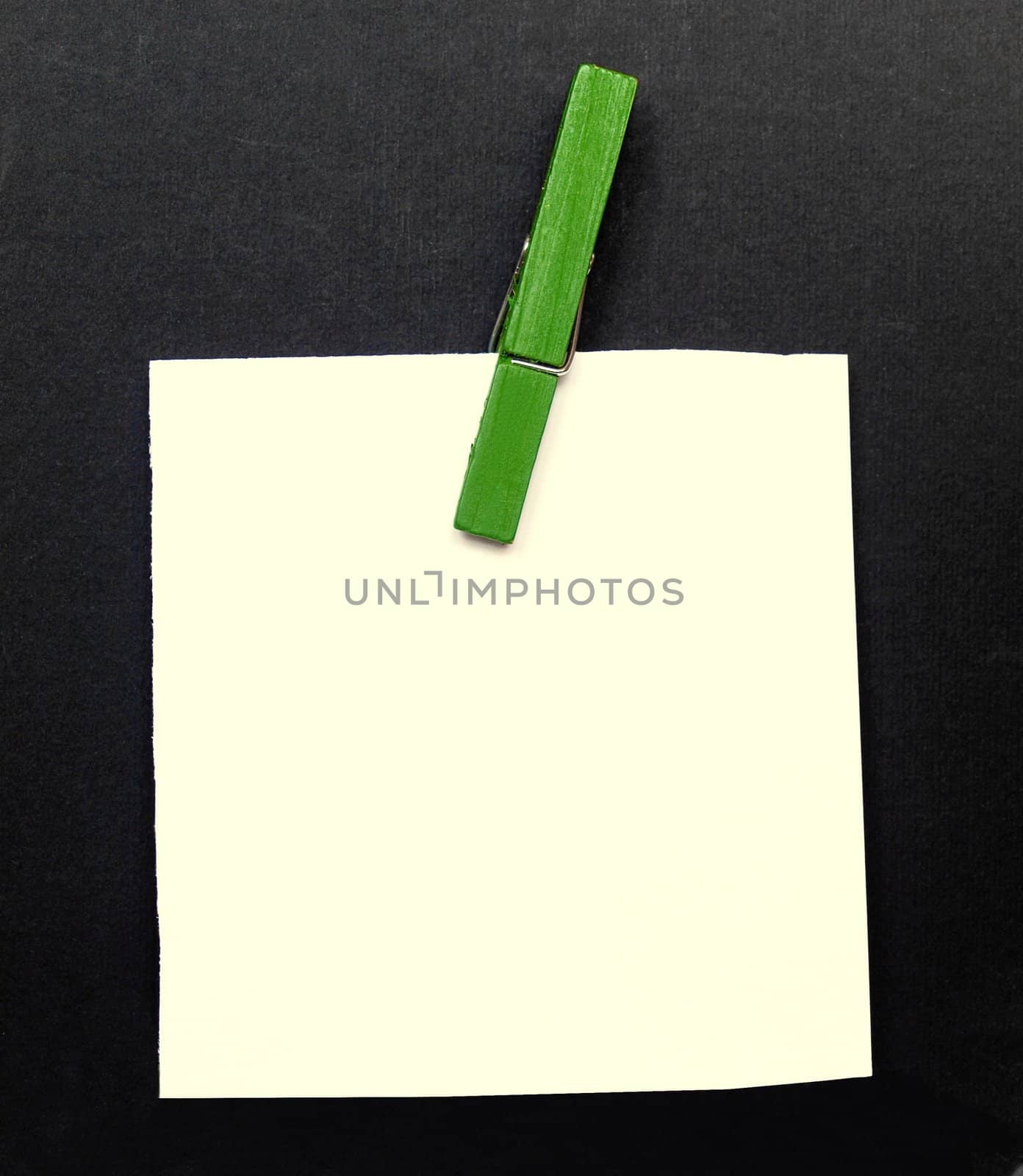 A blank notepad over a black background with a green clothespin