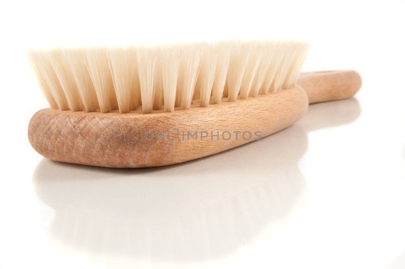 Close and low level of isolated wooden body brush arranged over white reflective surface.