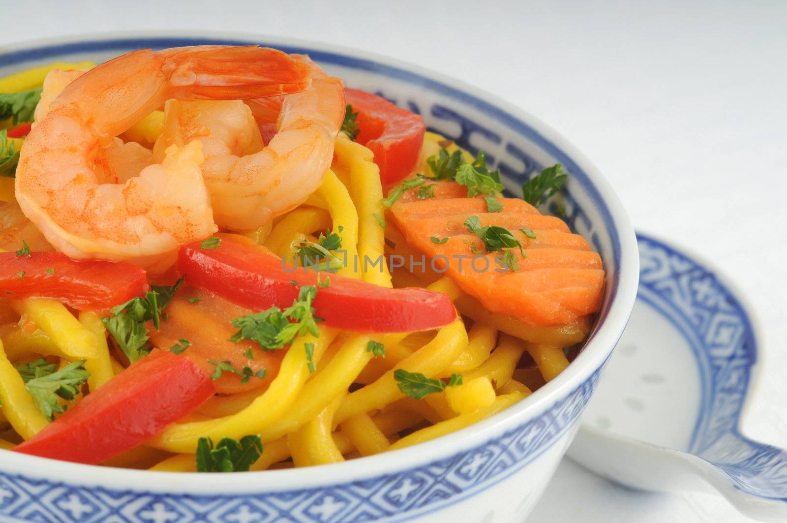 Bowl of chinese noodles with colorful shrimp and vegetables.