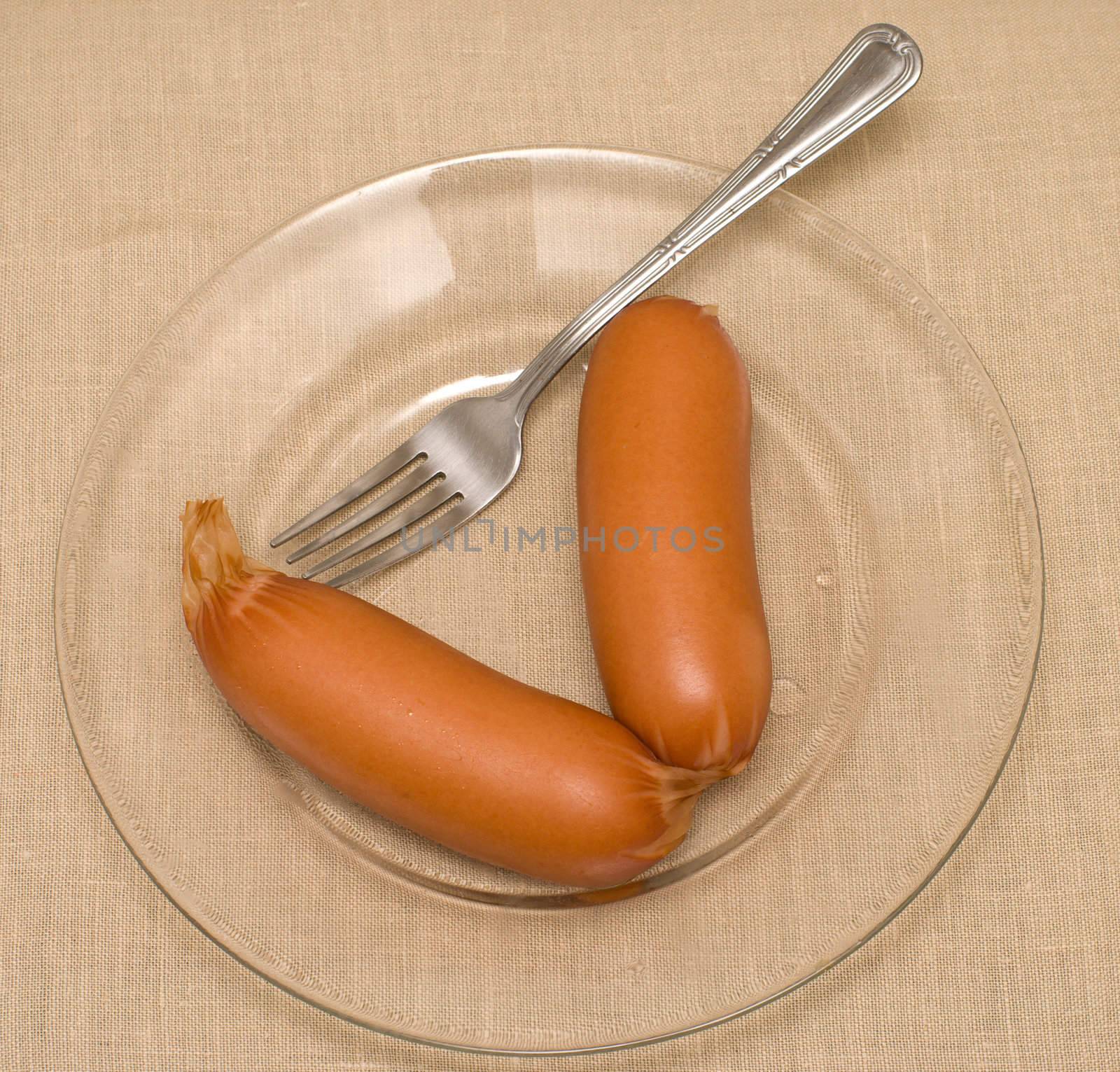 Sausages and a fork on a transparent plate.