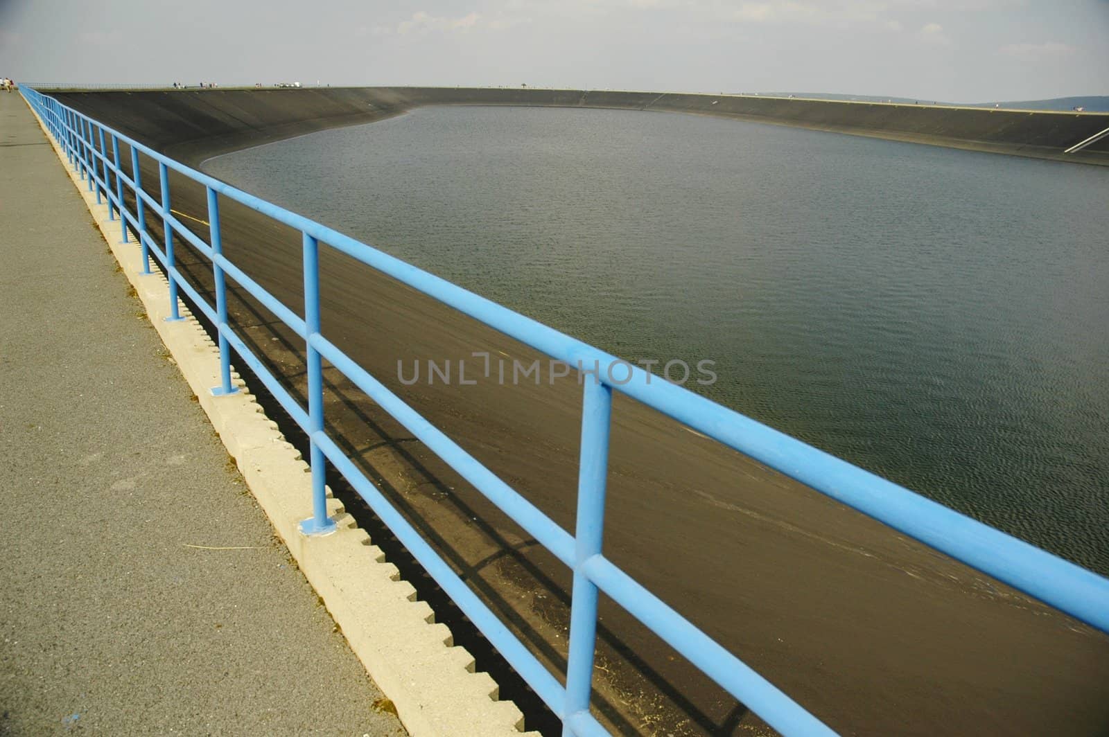 mountain lake, reservoir with safety rail, path and blue sky