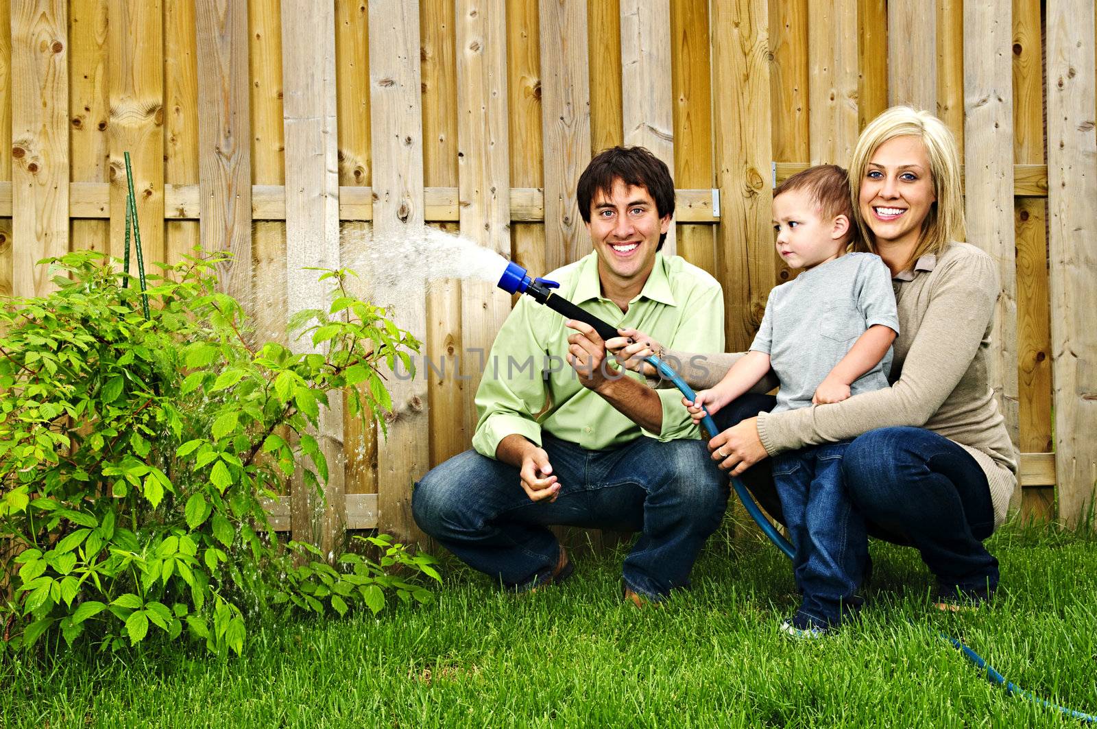 Happy family in backyard watering plant with hose