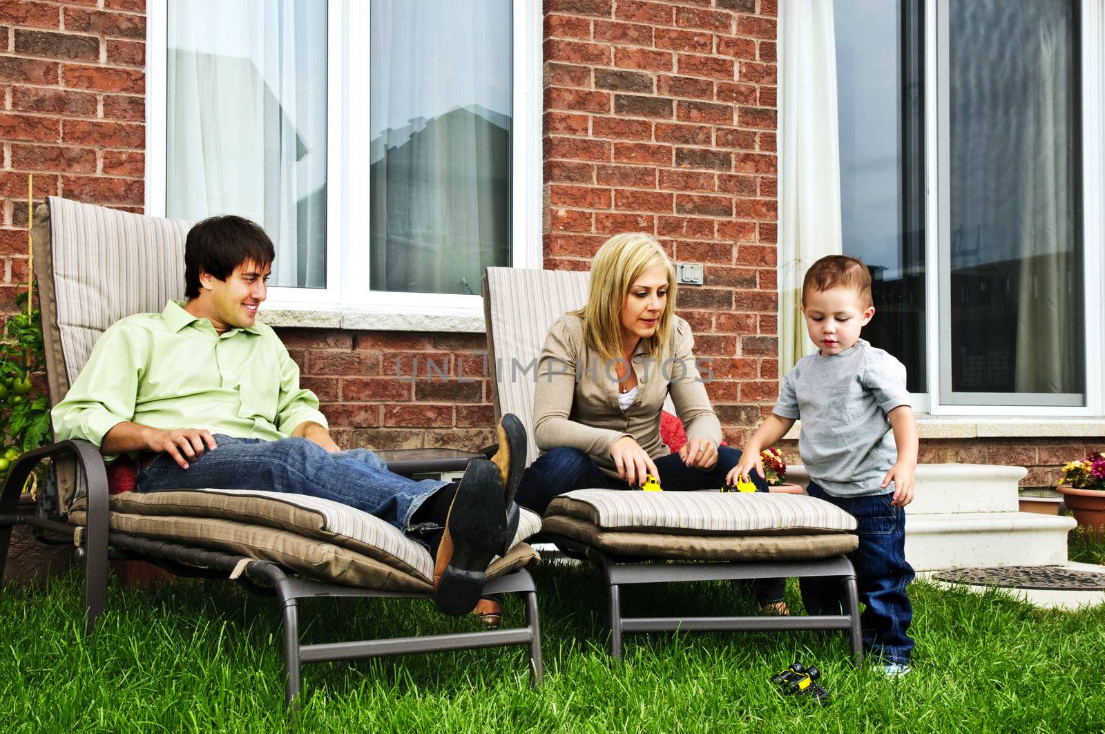 Happy family relaxing in backyard of new home with toddler