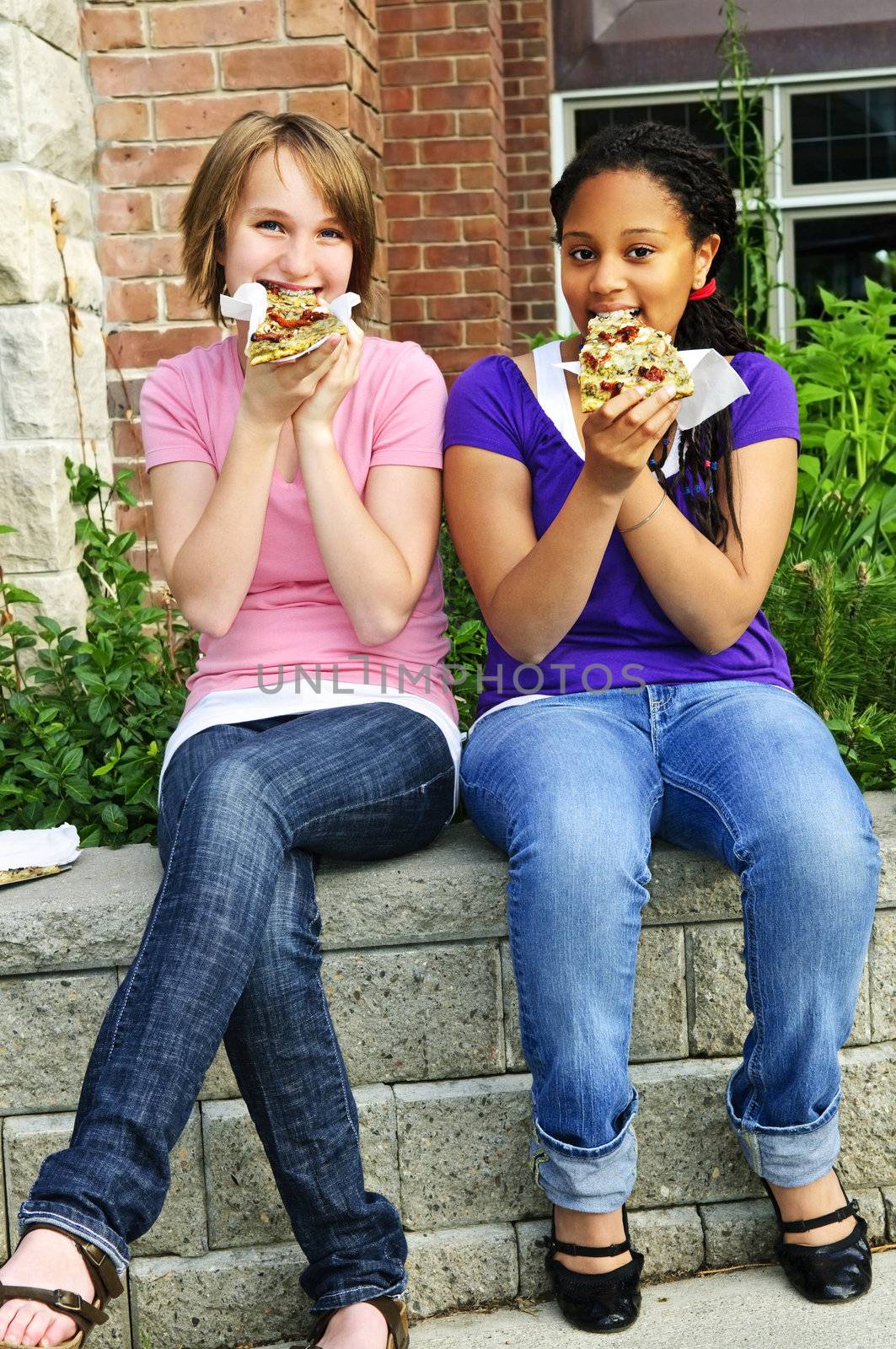 Two teenage girls sitting and eating pizza