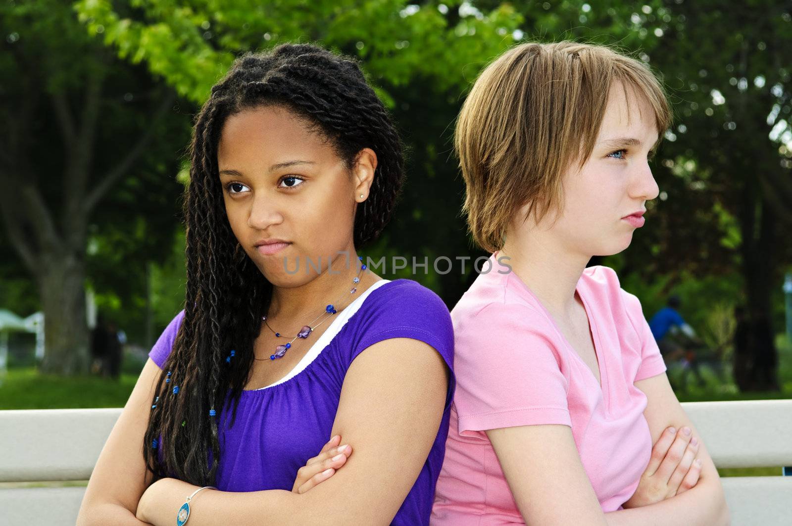 Two unhappy teenage girls sitting on bench
