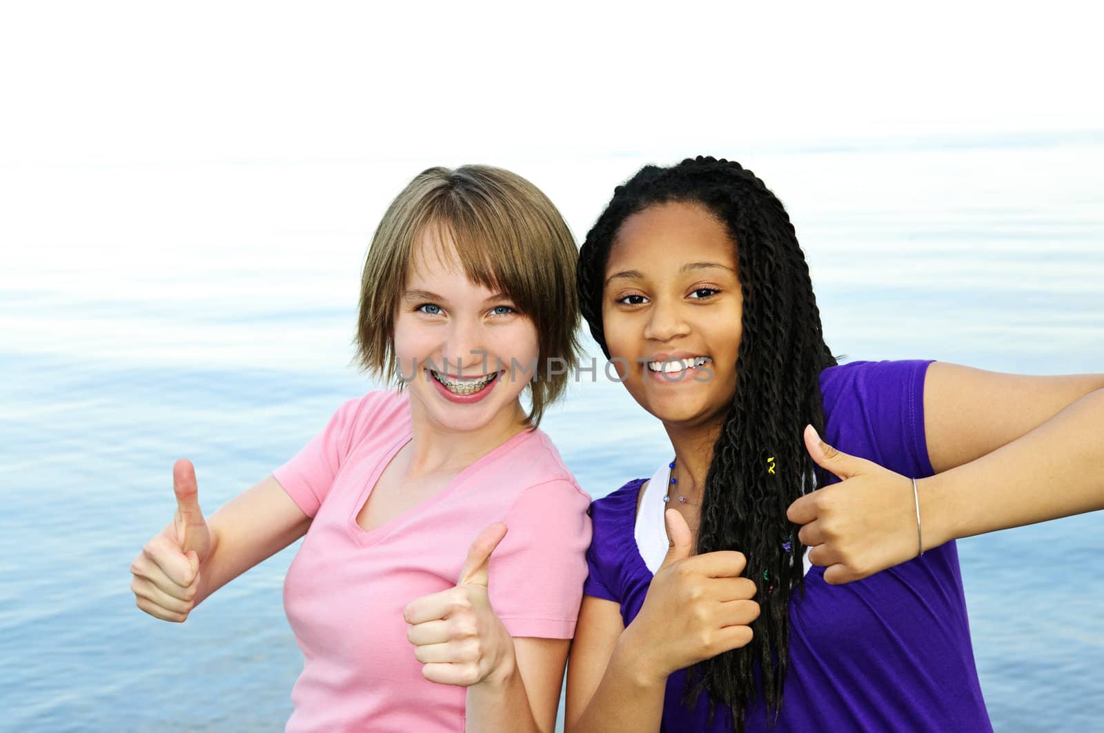 Portrait of two teenage girl friends showing thumbs up