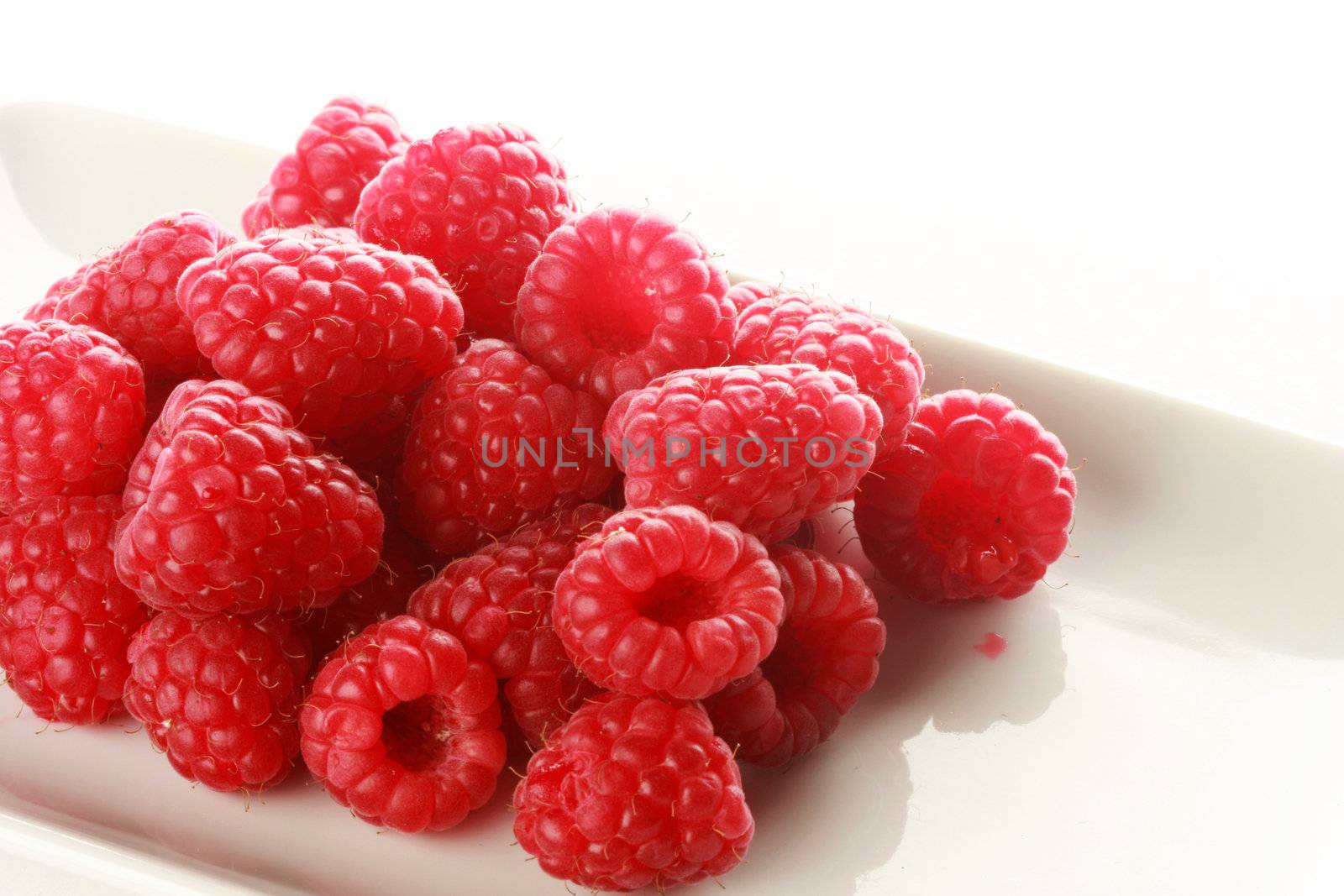 pile of raspberries on a white dish, isolated on white
