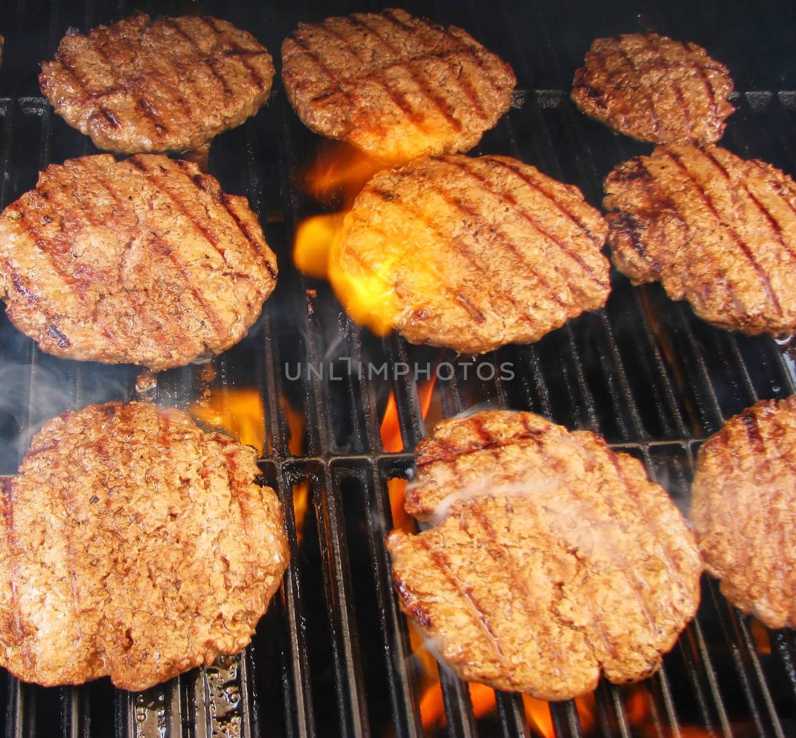 Cooking hamburgers on a grill with flames.
