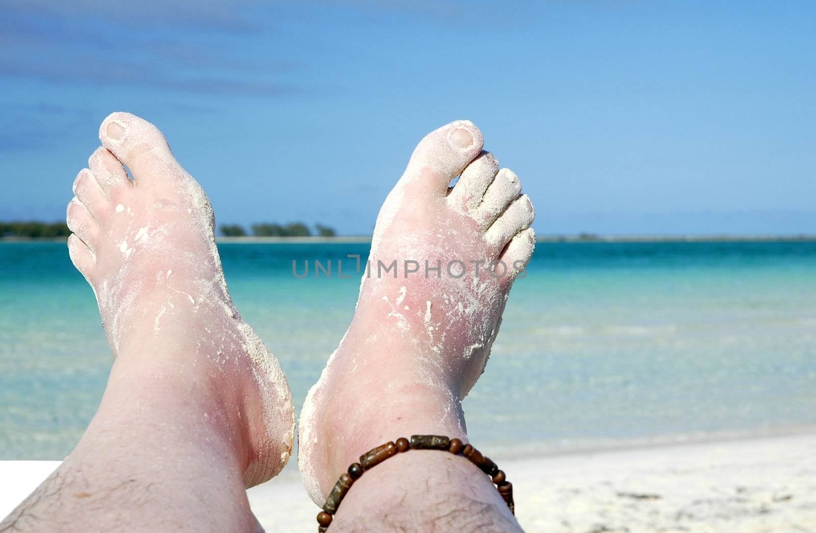 Bare feet covered in sand overlooking a blue sea.