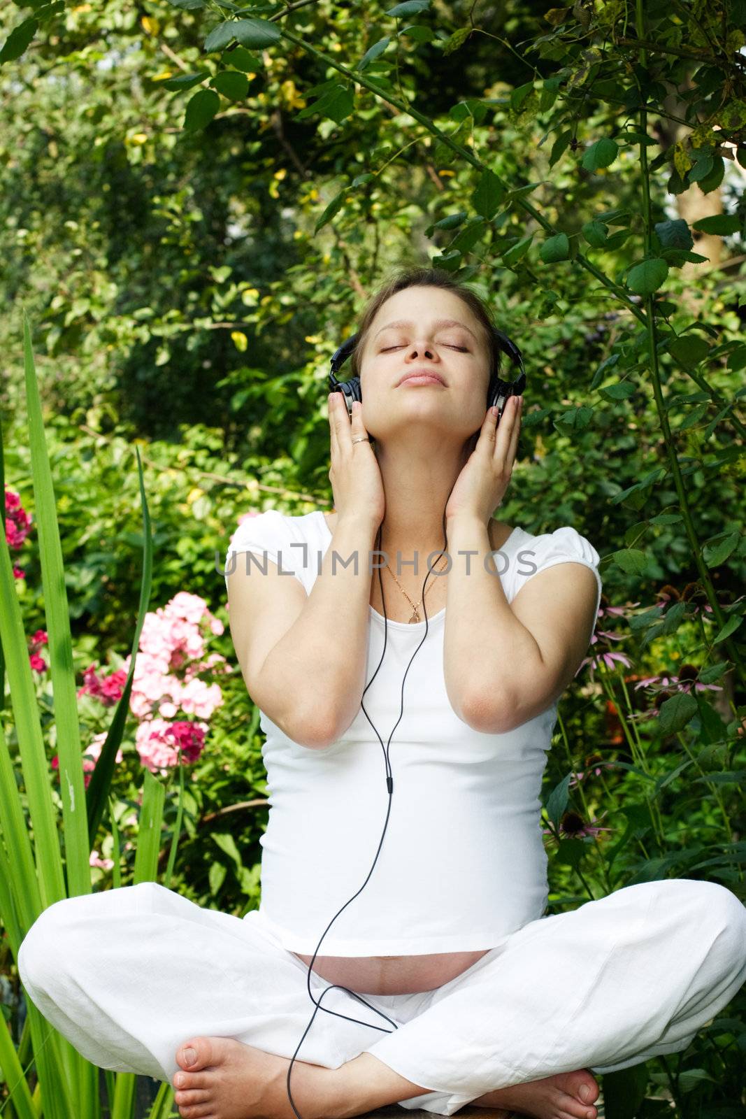 Young pregnant woman listening to a music at summer garden