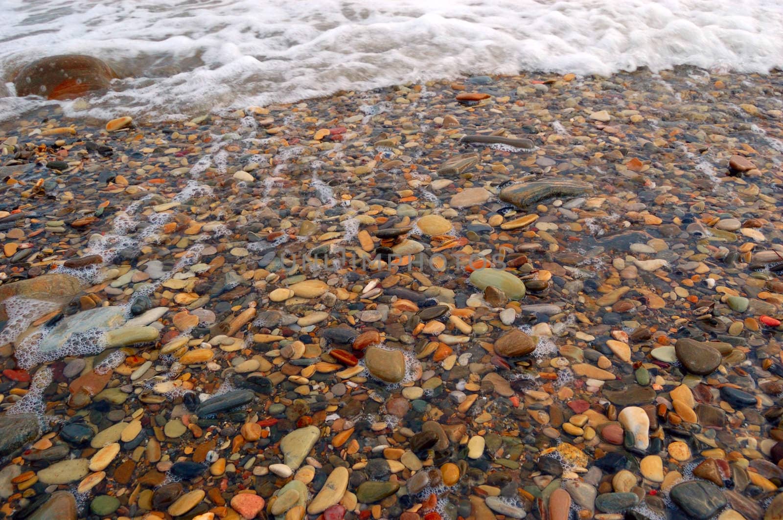 closeup of sea shore with pebbles covered with film of water