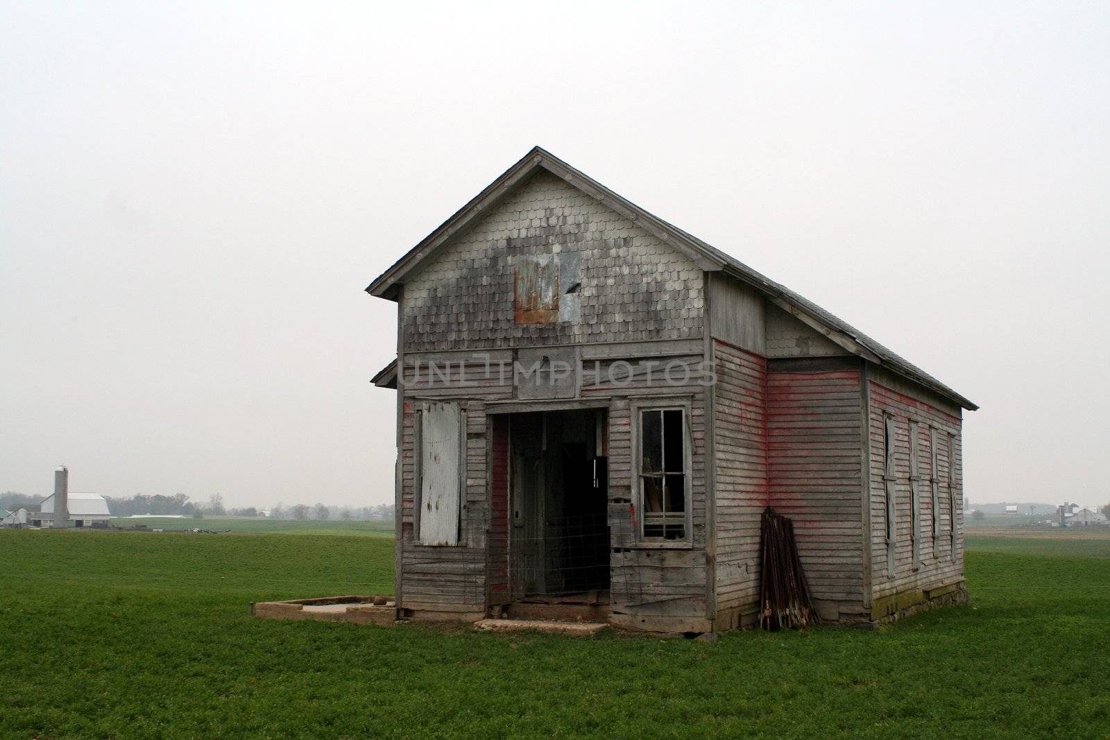 An old one room school house in a field on a cloudy day.